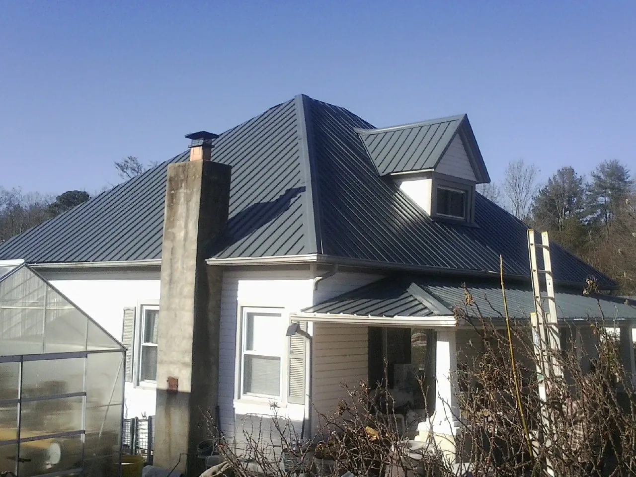 Dark blue standing seam metal roof on a white farmhouse with dormer — Slate & Tile Roof Repair by Roofing Brothers in Bryce