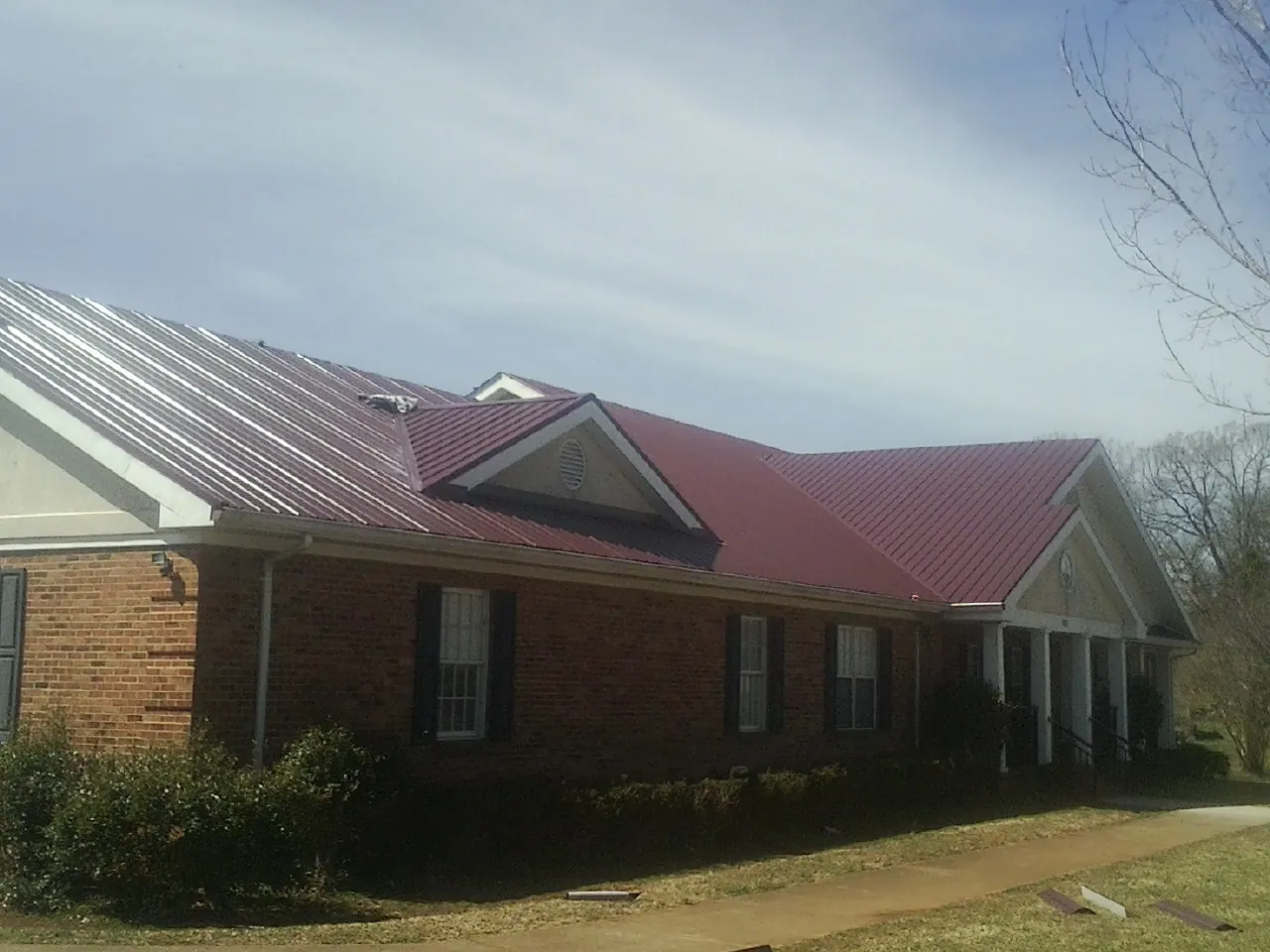 Red metal roof with gabled entries on a long brick building, from a Hail Damage Roof Repair job in Bryce