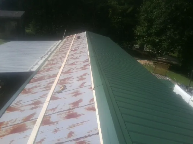 Old rusted panels beside newly installed green metal roofing — Wind Damage Roof Repair by Roofing Brothers in Bryce