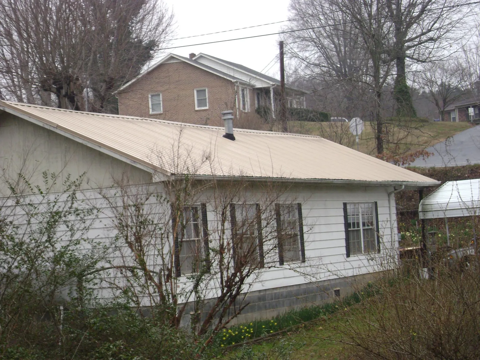 Tan metal roof on a white sided house set into a hillside — Commercial Roofing by Roofing Brothers in Bryce